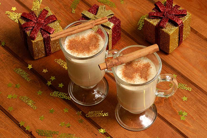 Two glass mugs containing dairy free eggnog decorated with cinnamon sticks.
Christmas drink