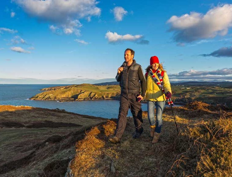 Couple walking above Porth Wen near Amlwch Wales Coast Path at sunset