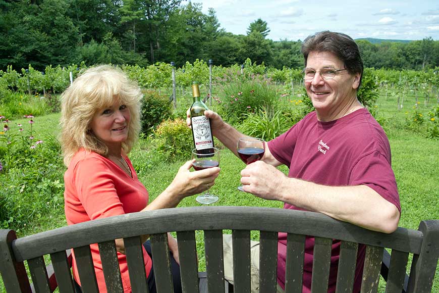 Roy and Nancy McGuill sitting on a bench holding wine glasses at Queen Bee Vineyard