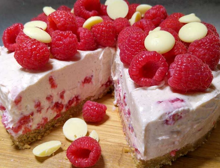 Raspberry and white chocolate vegan cheesecake topped with whole raspberries and white chocolate buttons