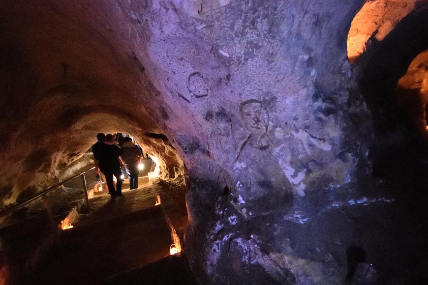 People carrying lanterns walking past wall carvings inside Baron's Cave in Reigate Surrey