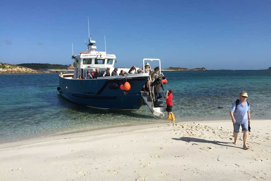 Passengers disembarking from the passenger ferry Firethorn of Bryher onto a sandy beach on the Isles of Scilly