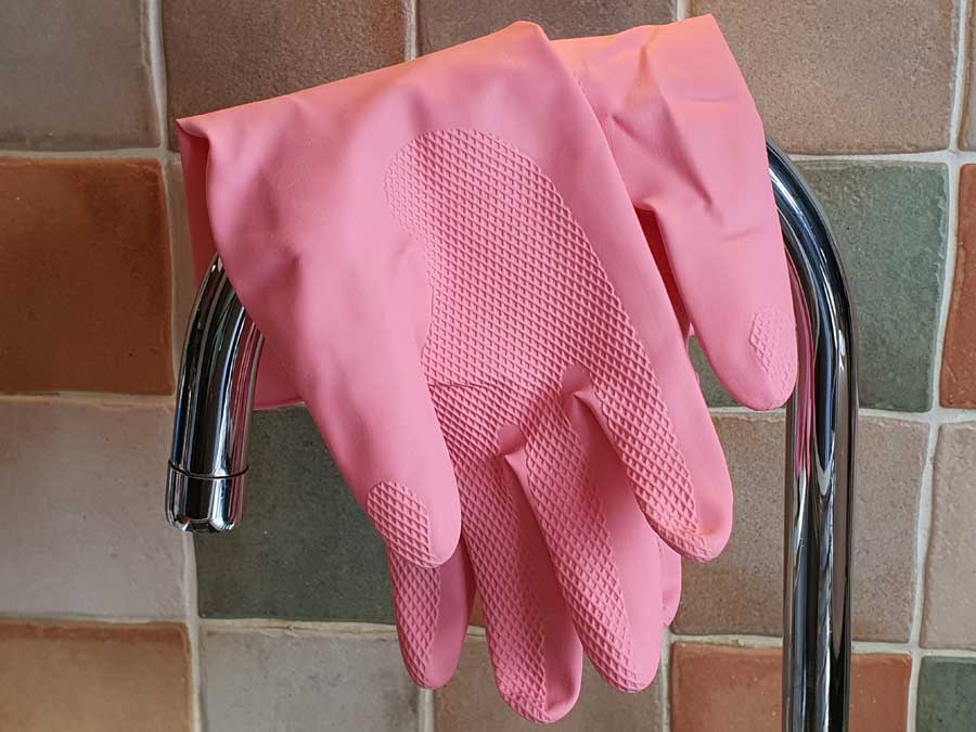 Pink rubber gloves hanging over kitchen tap