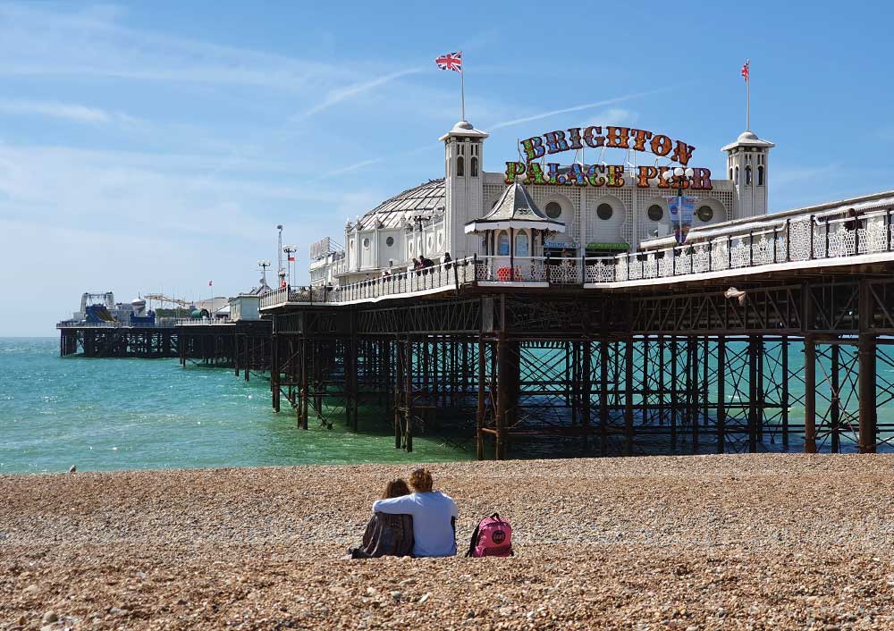 Couple sitting on the beach by Brighton Palace Pier