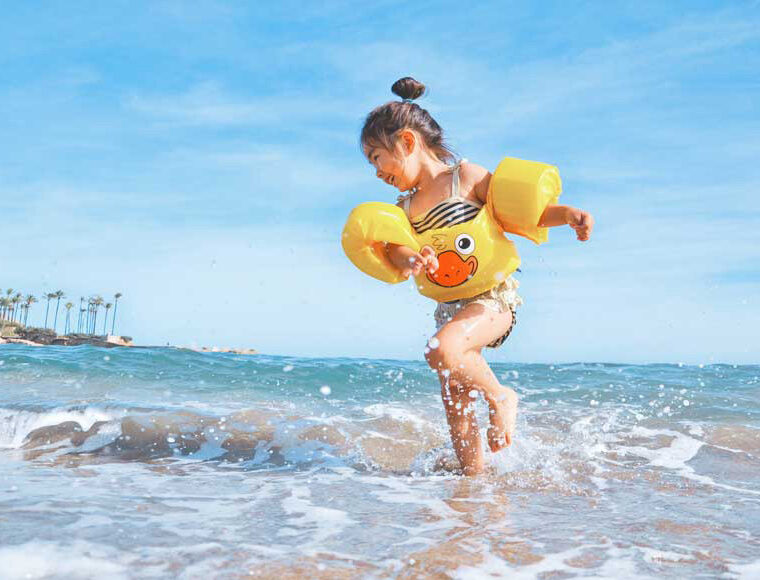 Young child wearing yellow buoyancy aids playing in the sea