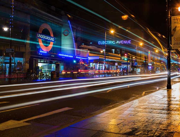 Night photo of Brixton showing neon lights and vehicle light trails outside the underground station