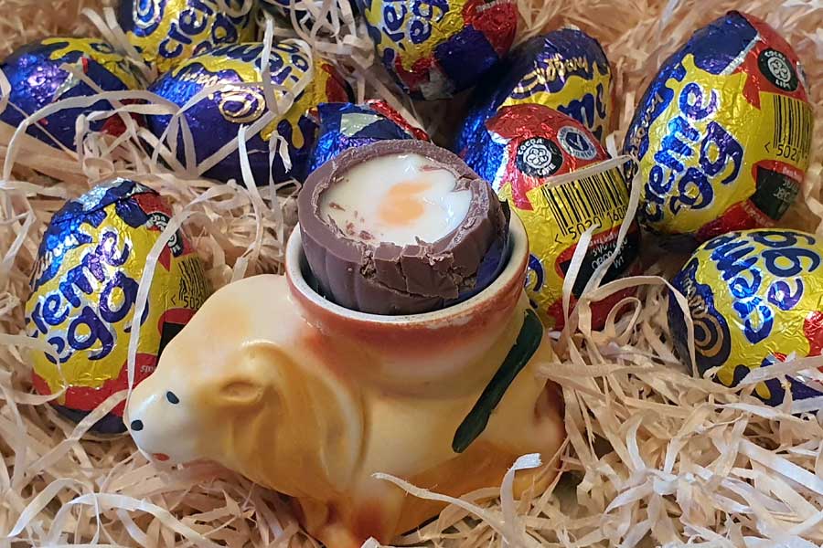 Cadbury chocolate and fondant creme eggs, one in lion shaped eggcup