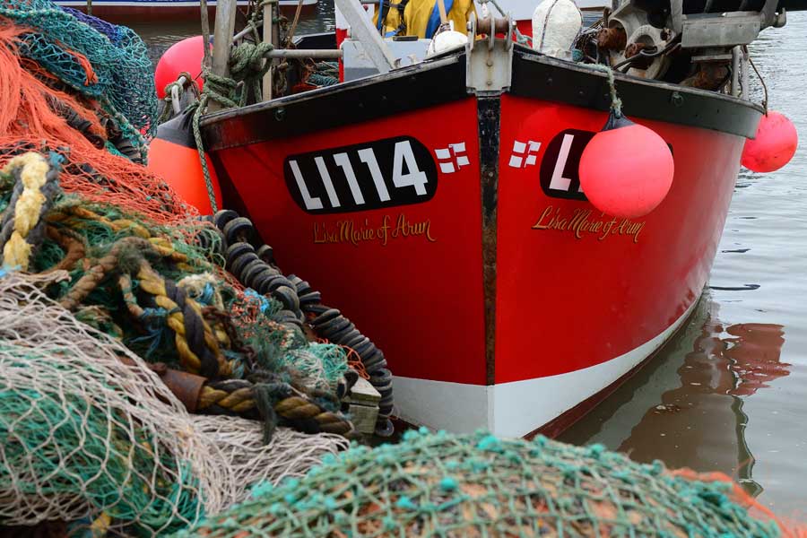 Fishing nets and bow of a bright red fishing boat moored at Whitstable Harbour in Kent
