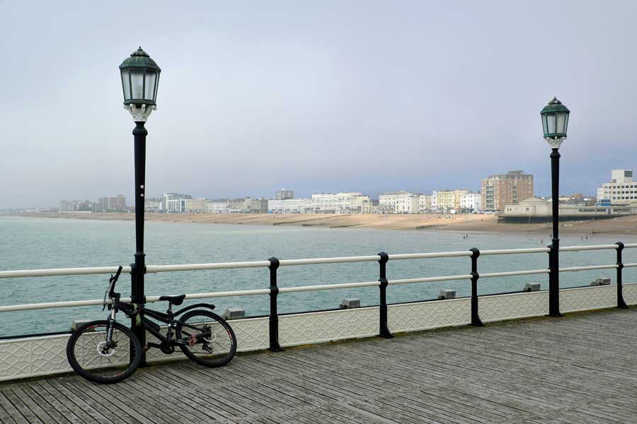 Bike leaning on railings of Worthing Pier with view of West Worthing, West Sussex UK