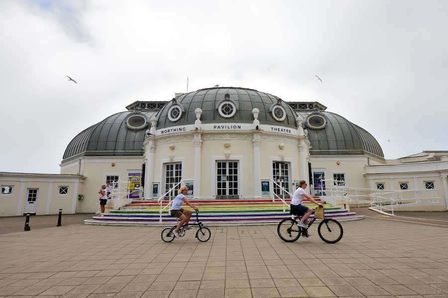 2 cyclists riding past Worthing Pavilion Theatre West Sussex UK