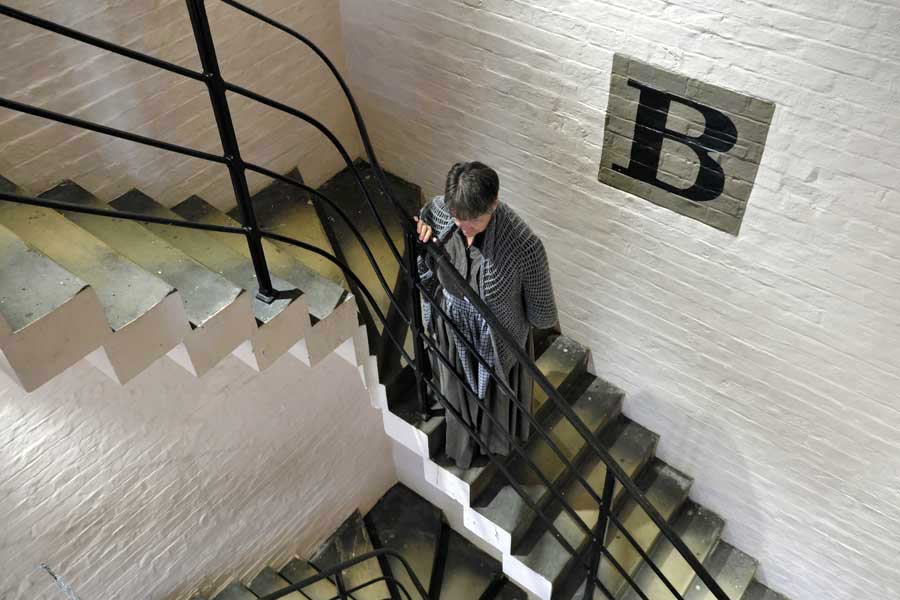 Female standing in stairwell wearing Victorian prison clothes at Lincoln Castle Victorian Prison Museum