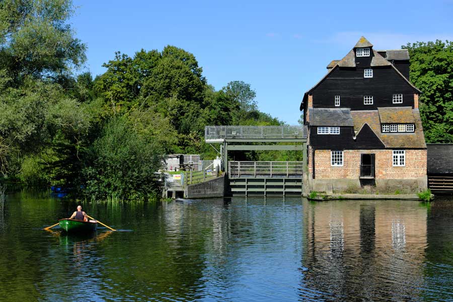 Person in green rowing boat on millpond and Houghton Mill in Houghton Cambridgeshire