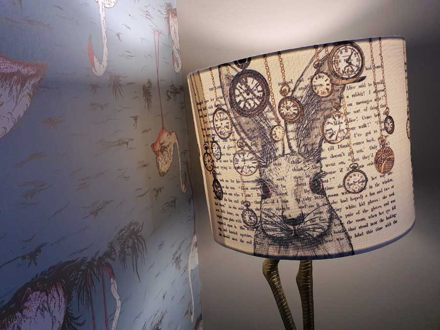 Lampshade showing watches and a rabbit's head next to flamingo wallpaper in Looking Glass Cottage, Brighton, UK
