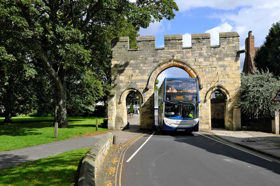 19th century reconstruction of the medieval Priory Arch, marking the entrance to Lincoln's cathedral quarter,with double decker bus passing through it