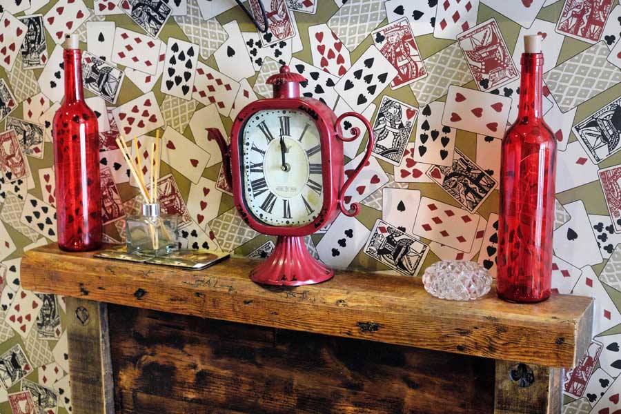 Playing card wallpaper and teapot clock on wooden mantelpiece at Looking Glass Cottage, Brighton, UK
