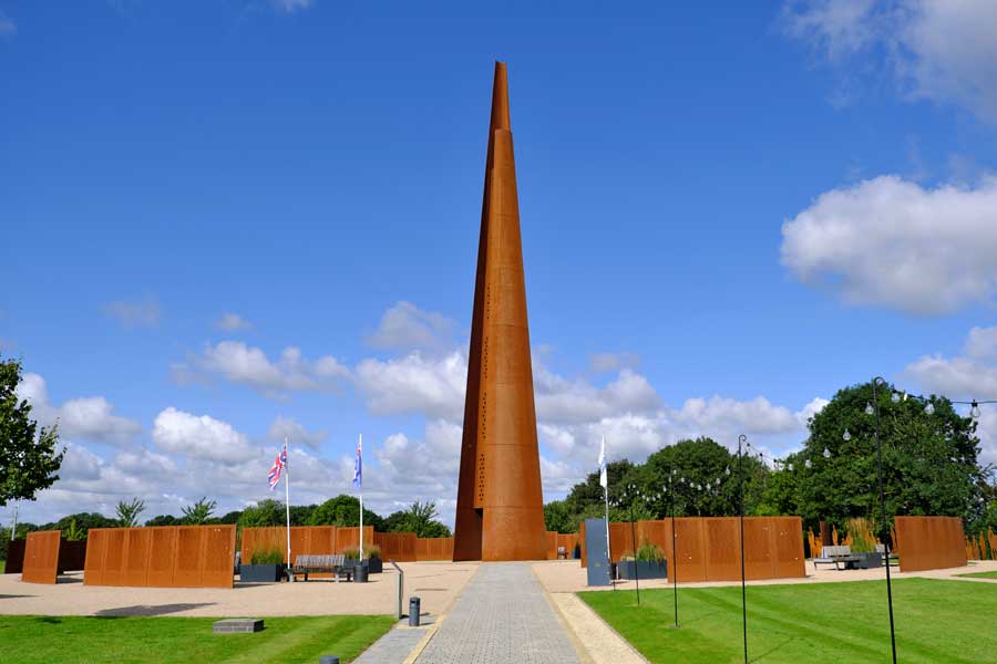 The Memorial Spire and Walls of Names at International Bomber Command Centre Lincoln photographed from the footpath against a blue sky and clouds