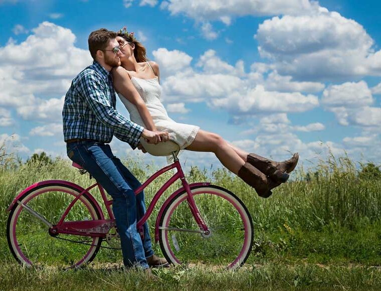 Male riding bicycle with female on handlebars in countryside