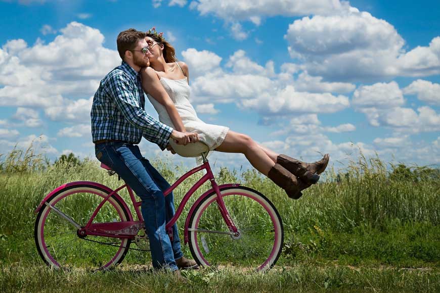 Male riding bicycle with female on handlebars in countryside