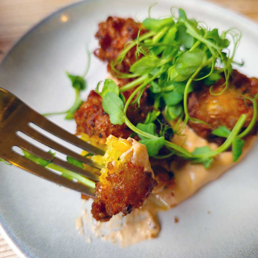 Sweetcorn fritters with sriracha yoghurt dressing on a plate topped with fresh rocket