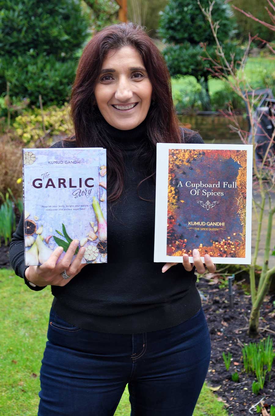 Kumud Gandhi standing outside holding her books The garlic story and A Cupboard Full of Spices