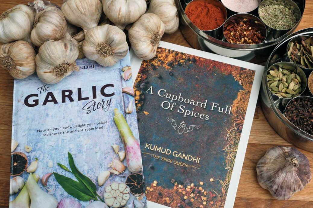The Garlic Story and A Cupboard Full of Spices recipe books by Kumud Gandhi surrounded by garlic and spices