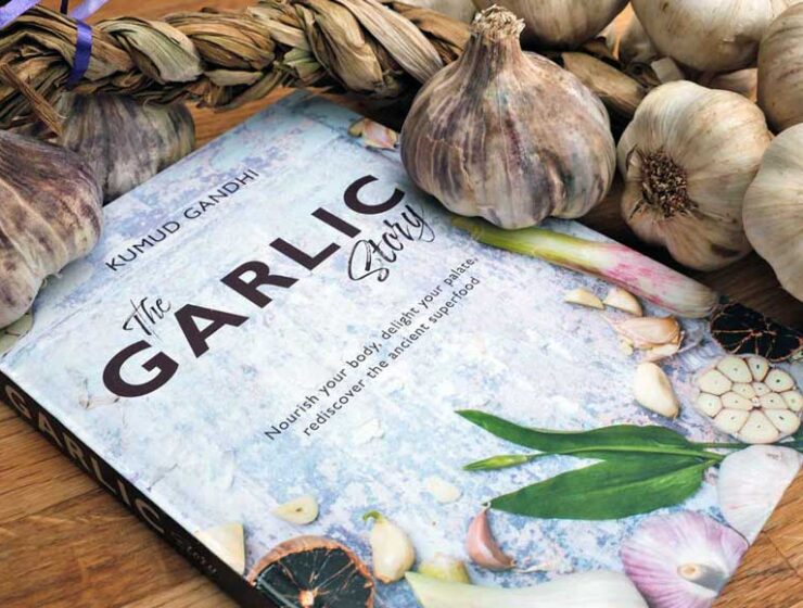 The Garlic story recipe book by Kumud Gandhi surrounded by garlic bulbs