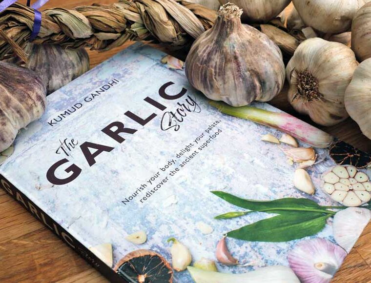 The Garlic story recipe book by Kumud Gandhi surrounded by garlic bulbs