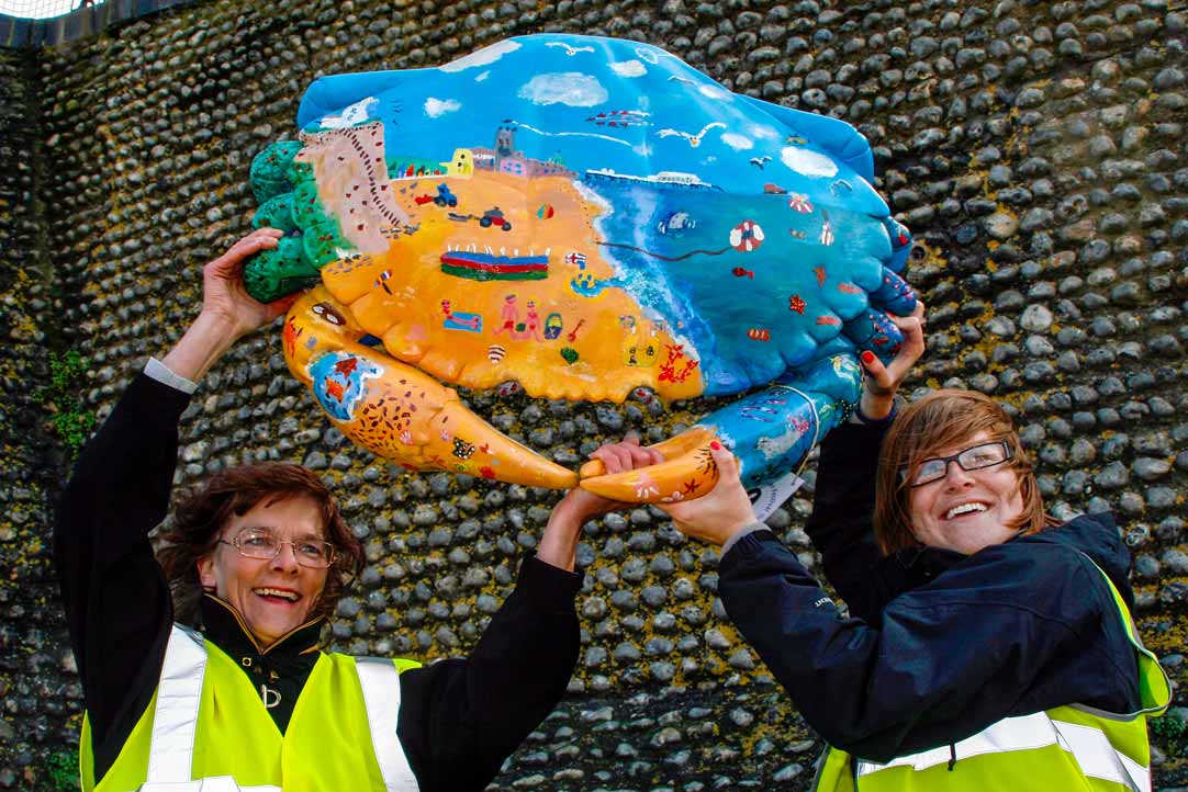 Two women holding up a large painted model crab