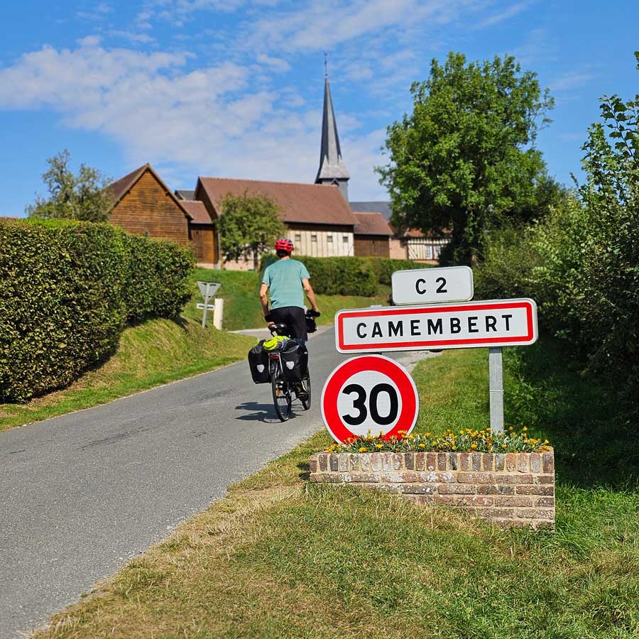 Cyclist riding past Camembert road sign Normandy France