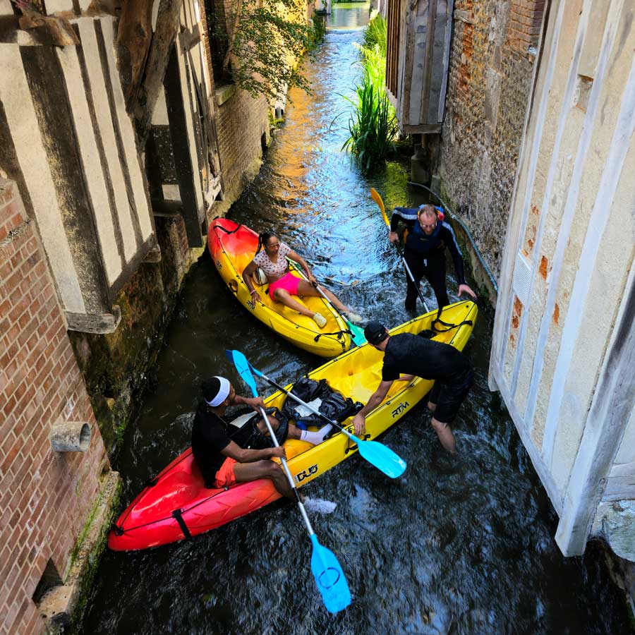 People navigating canoes on the canals that run between the buildings of Pont Audemer France
