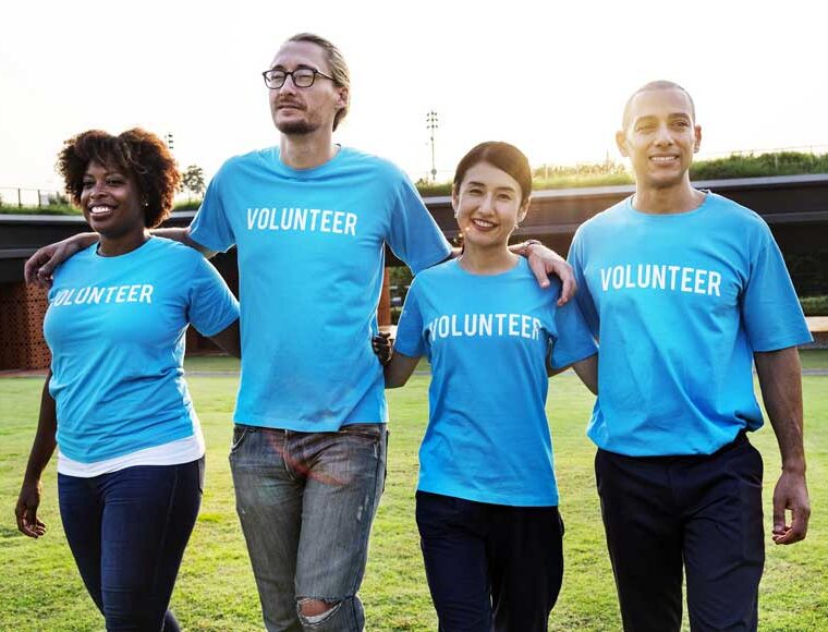 A group of multiethnicity volunteers walking together with their arms around shoulders on the grass in a park