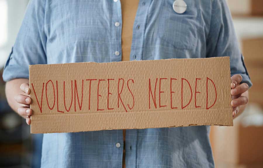 A person holding a cardboard sign with the inscription Volunteers Needed Volunteer Working Holidays