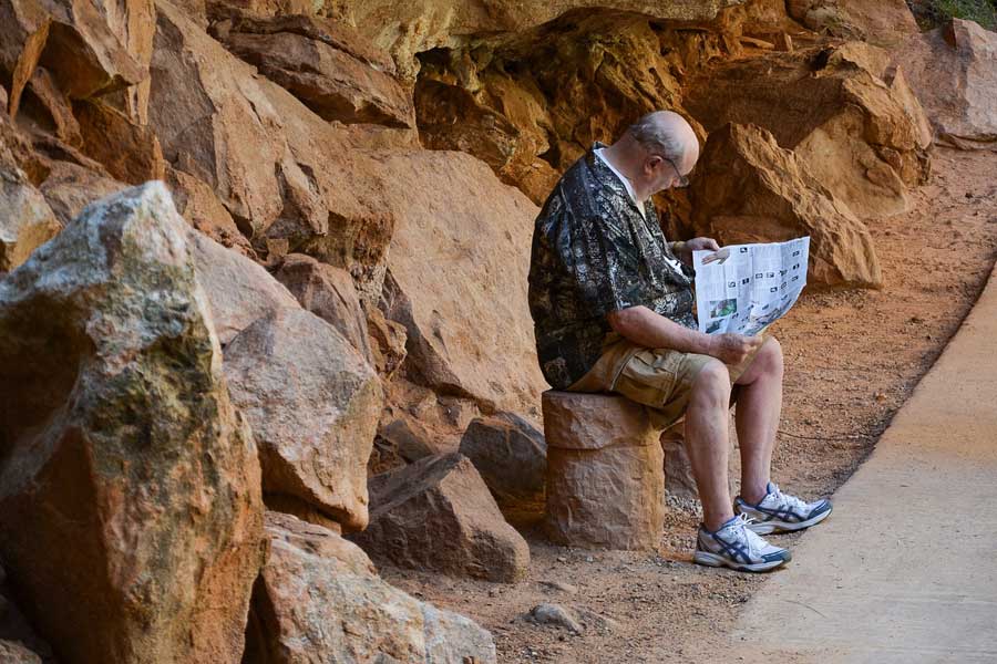 Man sitting on a rock reading a newspaper