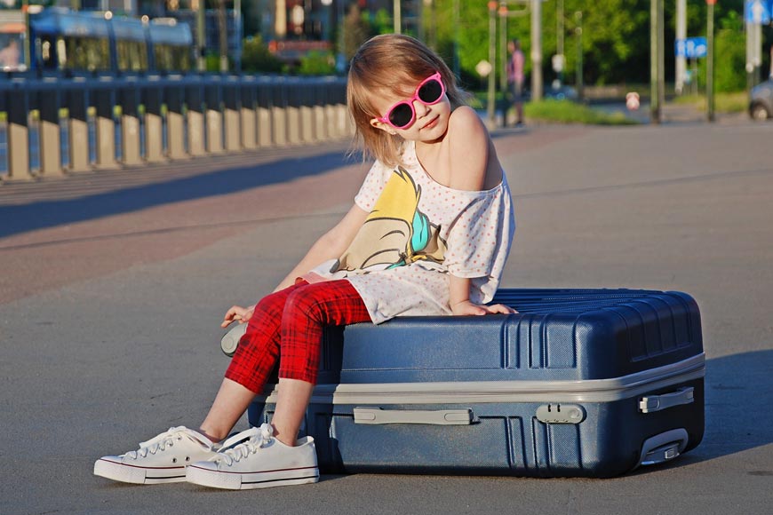 Child in summer clothes and sunglasses sitting on a suitcase