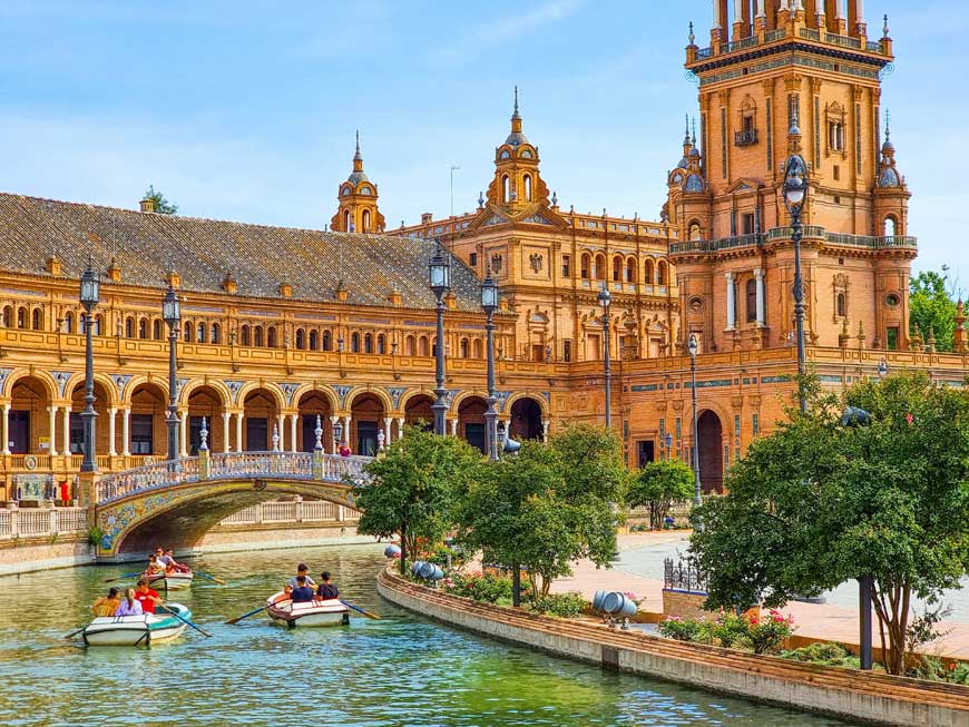 Group of people in rowing boats on a river in front of a large building 
Plaza España, Seville, Spain
