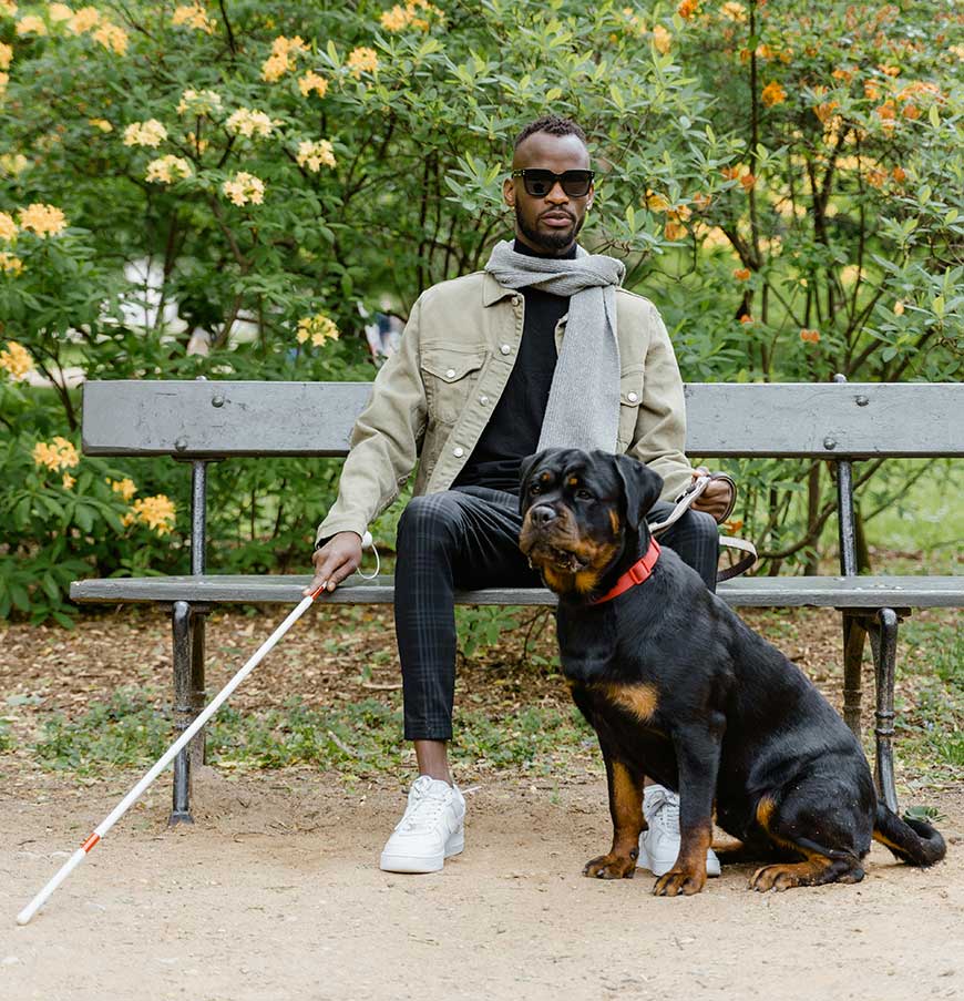 Man with a cane sitting on a Bench Beside a Guide Dog.

Accessible travel