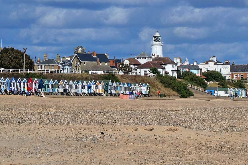 View from the beach of the brightly coloured beach huts, town and lighthouse in Southwold Suffolk