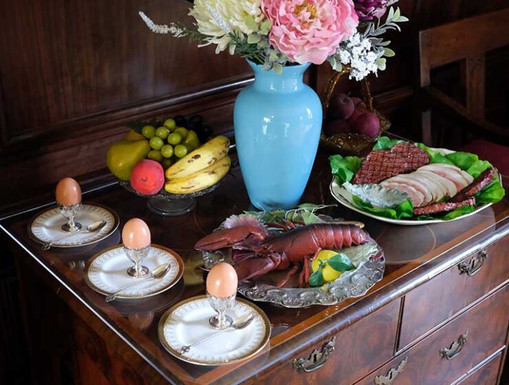 Sideboard set with Edwardian imitation food, boiled eggs, lobster, fruit, cooked meats, and a vase of flowers in the dining room at Preston Manor, Brighton