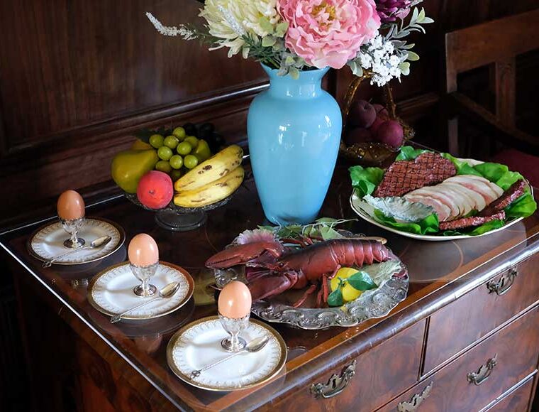 Sideboard set with Edwardian imitation food, boiled eggs, lobster, fruit, cooked meats, and a vase of flowers in the dining room at Preston Manor, Brighton