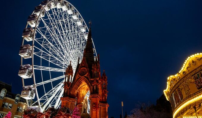 Festive setup at Albert Square in Manchester, UK, featuring the Manchester Christmas Markets with a giant Ferris wheel, an illuminated carousel, and the Prince Albert Memorial spire