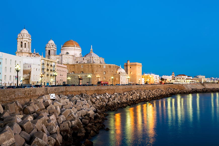 Cádiz Cathedral glowing at dusk along the coastal seawall in Cádiz, Spain