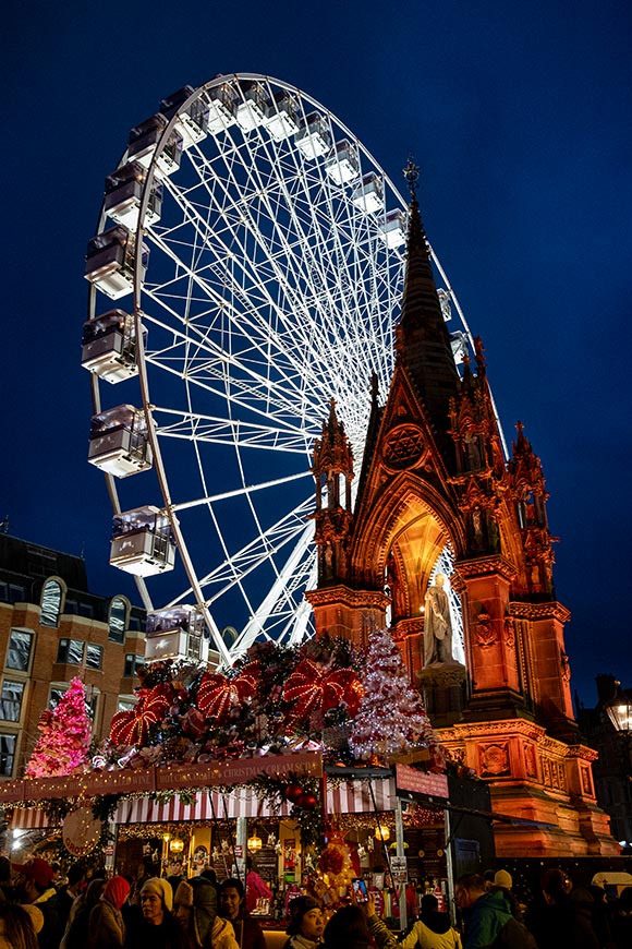 Festive setup at Albert Square in Manchester, UK, featuring the Manchester Christmas Markets with a giant Ferris wheel, stalls, and the Prince Albert Memorial spire.