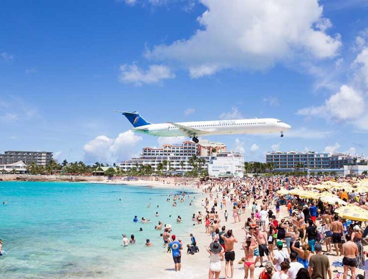 Aircraft flying across a crowded beach at Maho Beach in Sint Maarten approaching the runway at Princess Juliana International Airport.