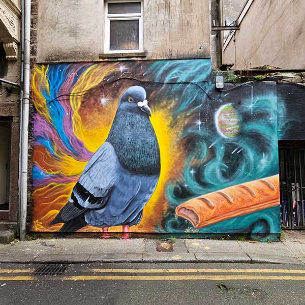 Large mural of a pigeon and a sausage roll with a cosmic style background on a wall in Back Crescent Street Morecambe Lancashire UK. Mural by Matty Green