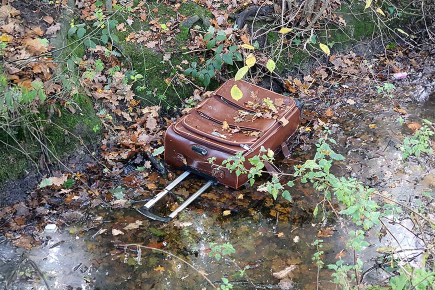 A brown suitcase discarded in a stream