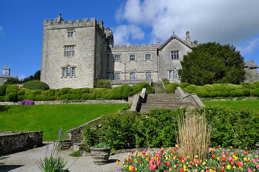 Looking towards Sizergh Castle in the Lake District on a sunny day, across tulip beds, grass banks and stone steps