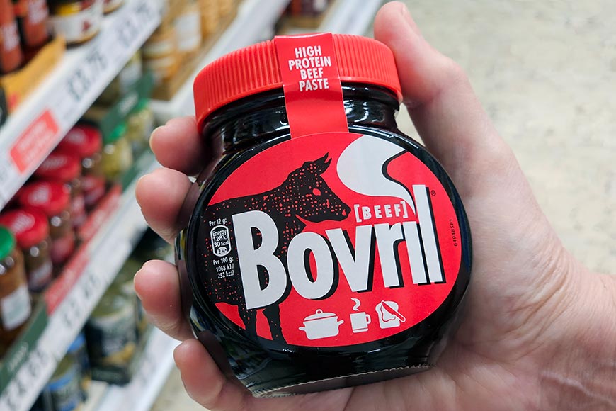 A hand holding a jar of Bovril near a supermarket shelf