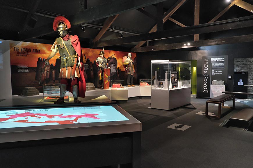 Life-size Roman legionary mannequins with armor and weapons in a museum display hall.