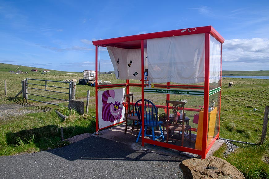 Bus shelter with a red frame and white curtains in a grassy field; banners and chairs are arranged inside and outside the structure.
