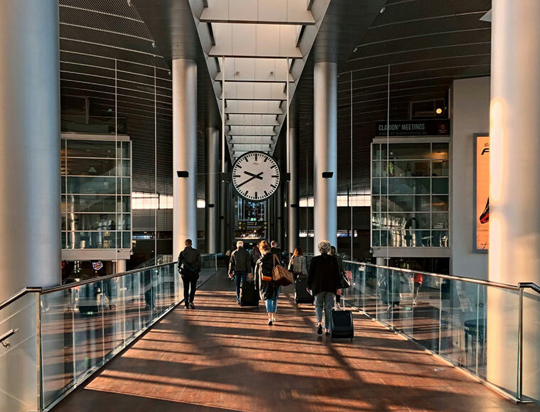 Image shows the interior hallway of Copenhagen Airport in Denmark, featuring a large analogue clock hanging from the ceiling